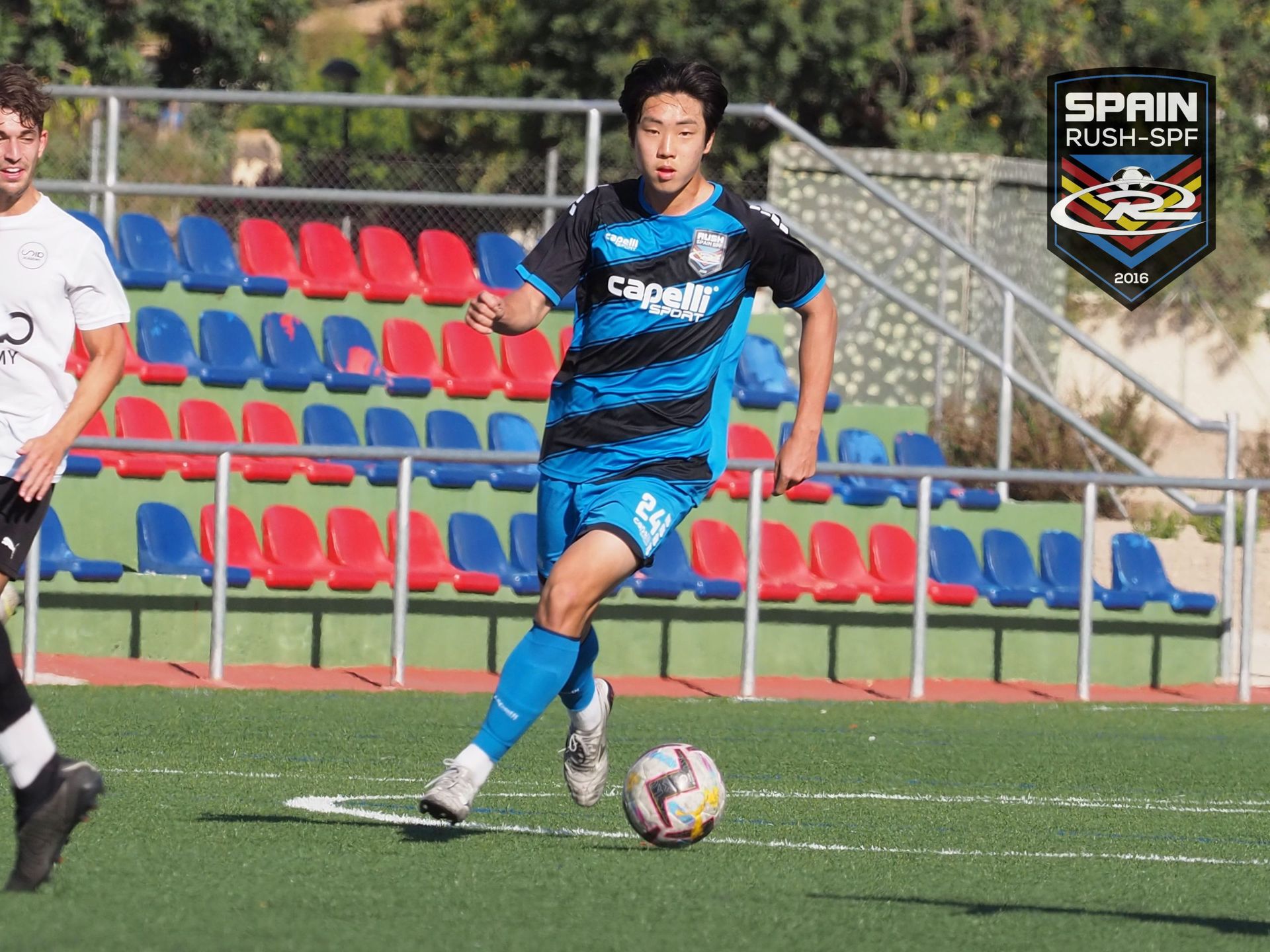 A man in a blue and black jersey is playing soccer on a field.