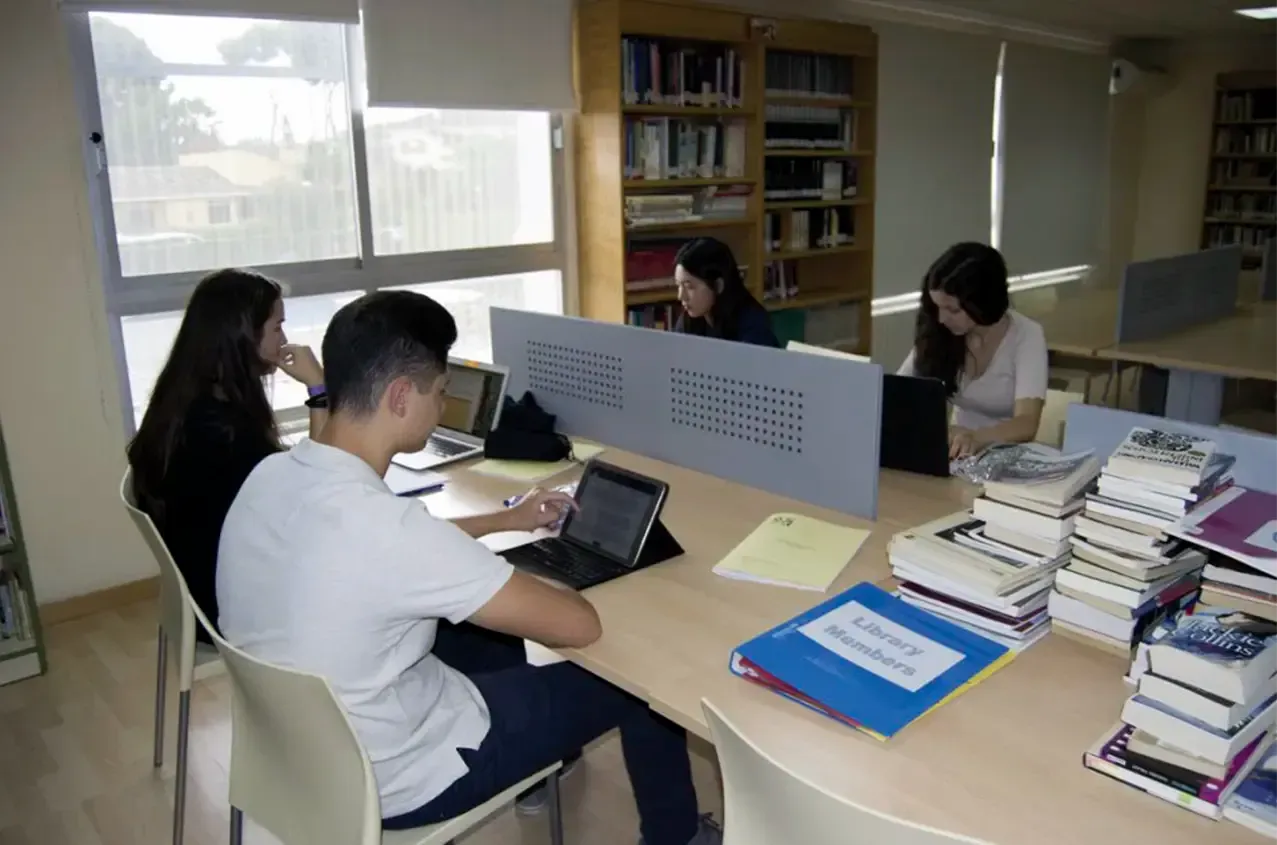 A group of people are sitting at a table with books and laptops.