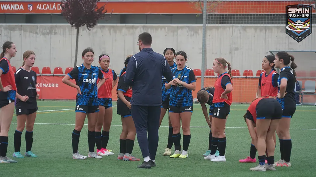 A group of female soccer players are standing in a huddle on a field.