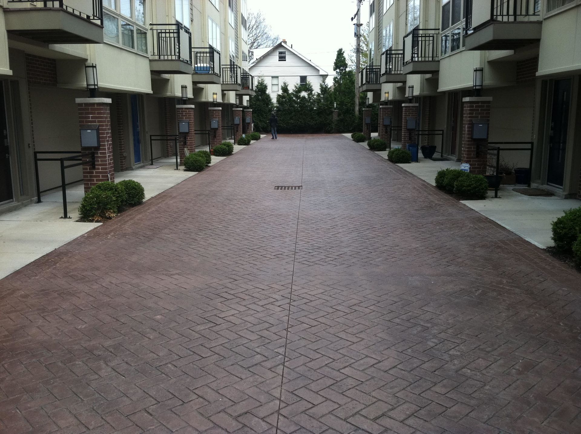 A brick-paved alleyway between apartment buildings, with a small house visible at the end.