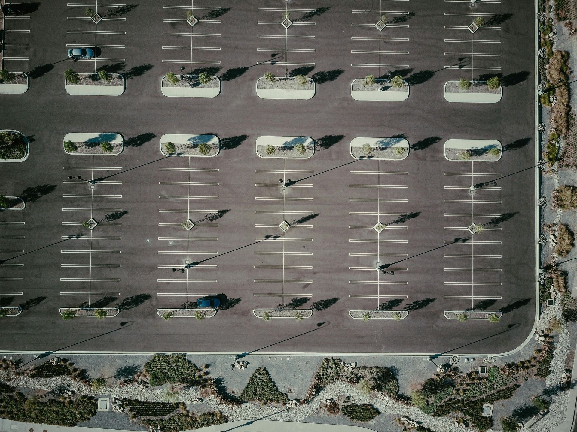 Aerial view of an empty asphalt parking lot with white parking lines and small landscaped medians.
