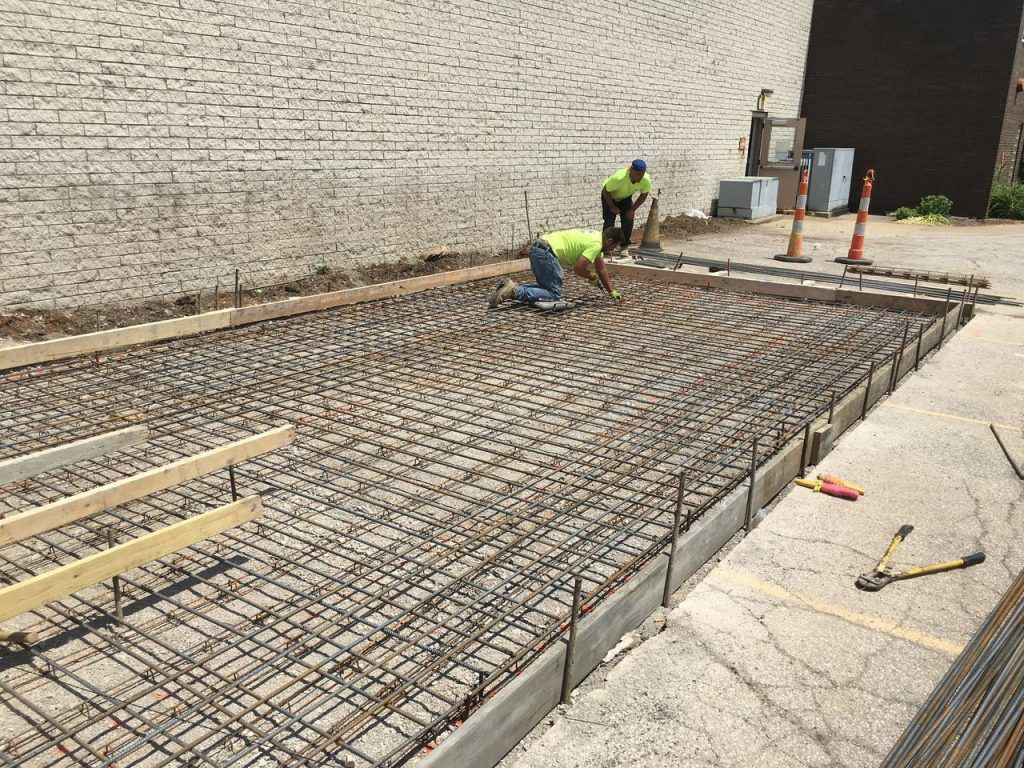 Construction workers pouring concrete into a rebar-filled formwork, outdoors.