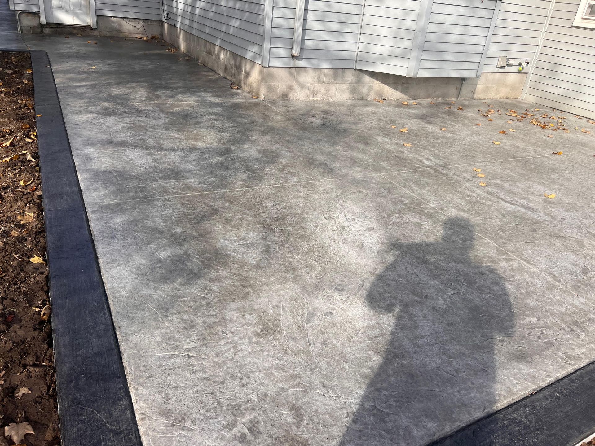Concrete patio next to a house, with a black border and a person's shadow visible.