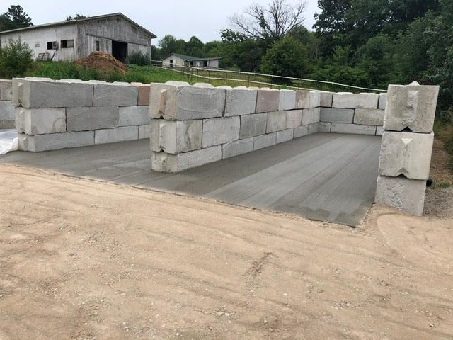 Concrete block walls framing a concrete floor, on a dirt lot. Buildings and trees in the background.