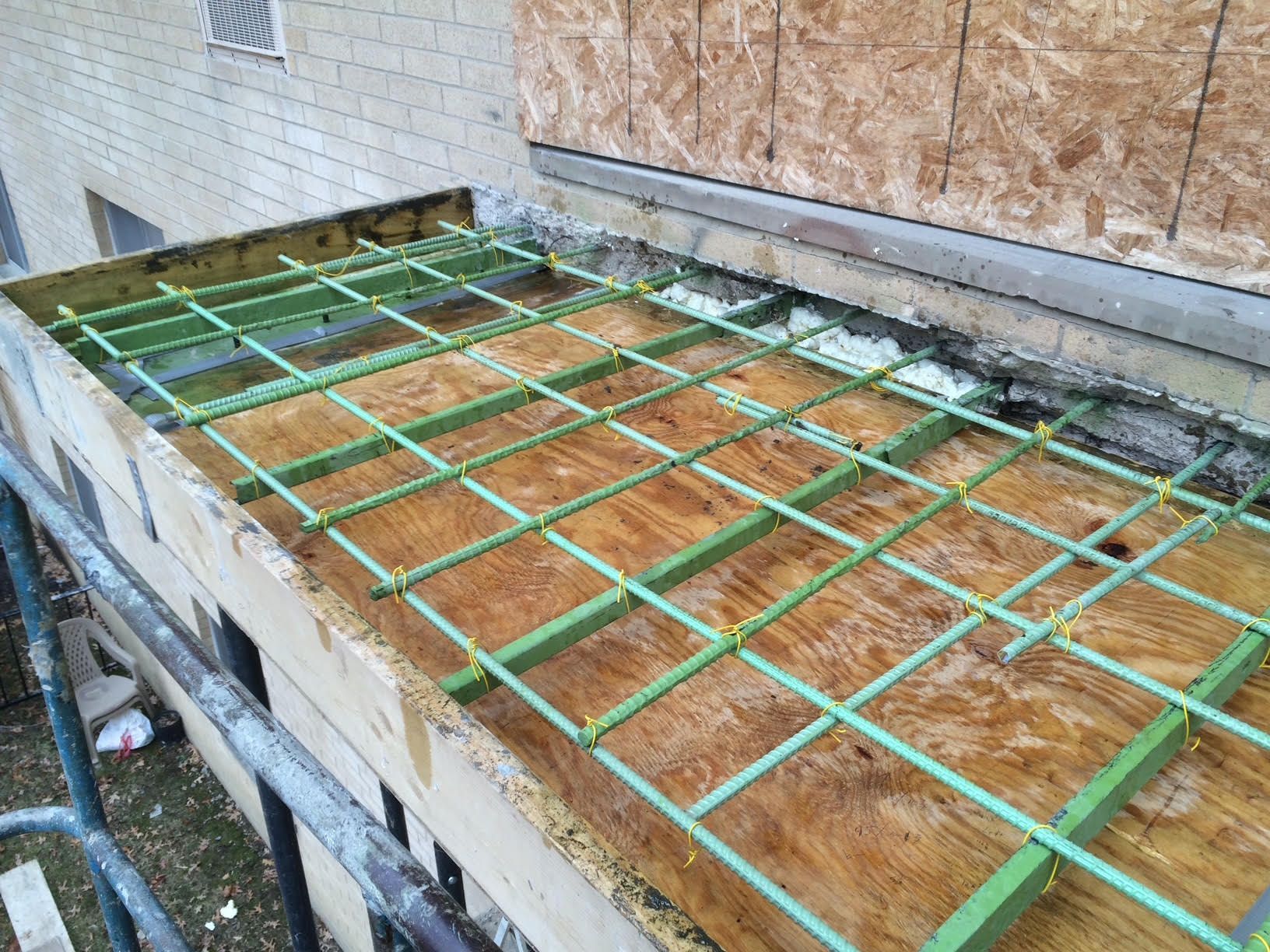 Construction site: A wooden formwork with a green rebar grid laid on top, ready for concrete pouring.