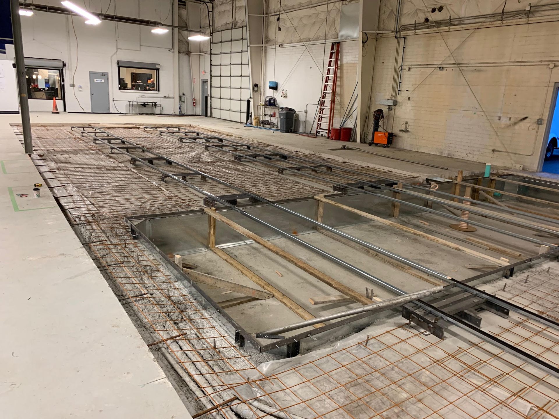 Construction site with exposed rebar and concrete, likely a warehouse or industrial space. Floor appears to be undergoing renovation.