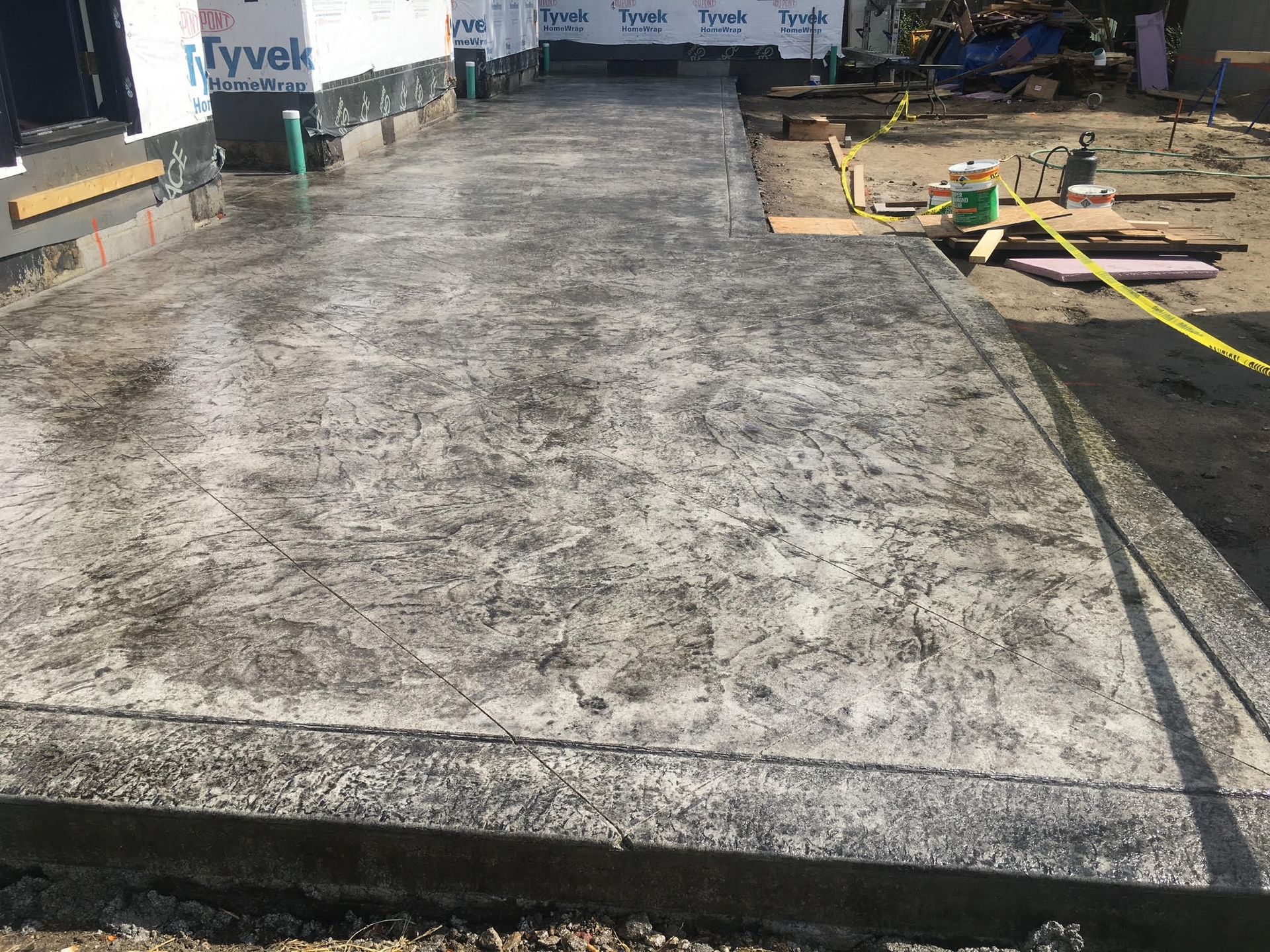 Newly poured concrete patio in front of a building under construction; gray with textured finish.