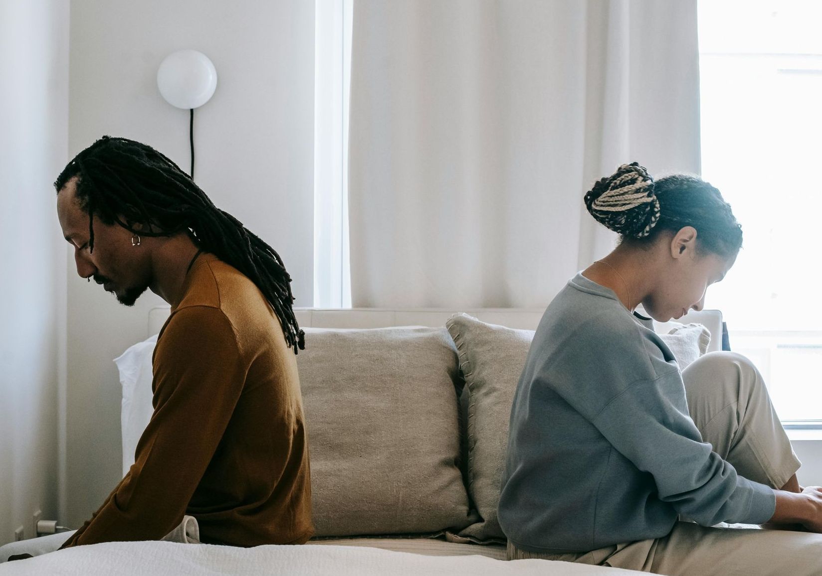 A man and a woman are sitting back to back on a couch.