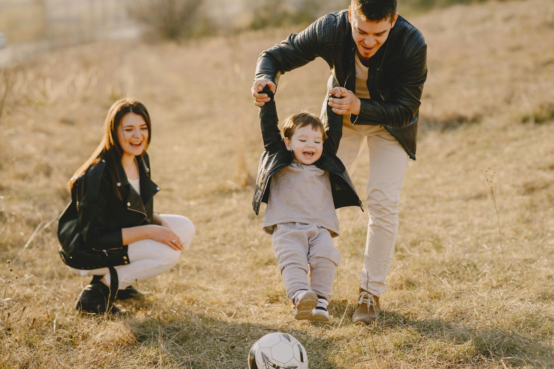 An unmarried couple is playing with a soccer ball in a field.