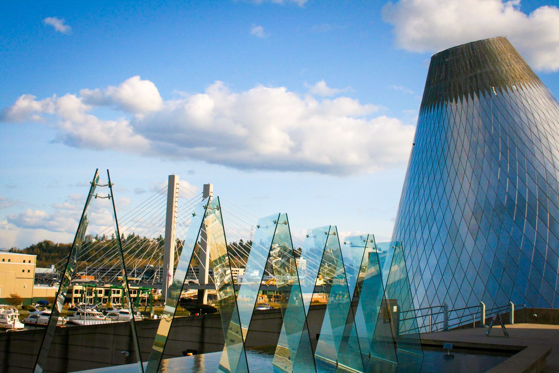 Modern building with conical roof and geometric glass sculptures, blue sky and clouds.