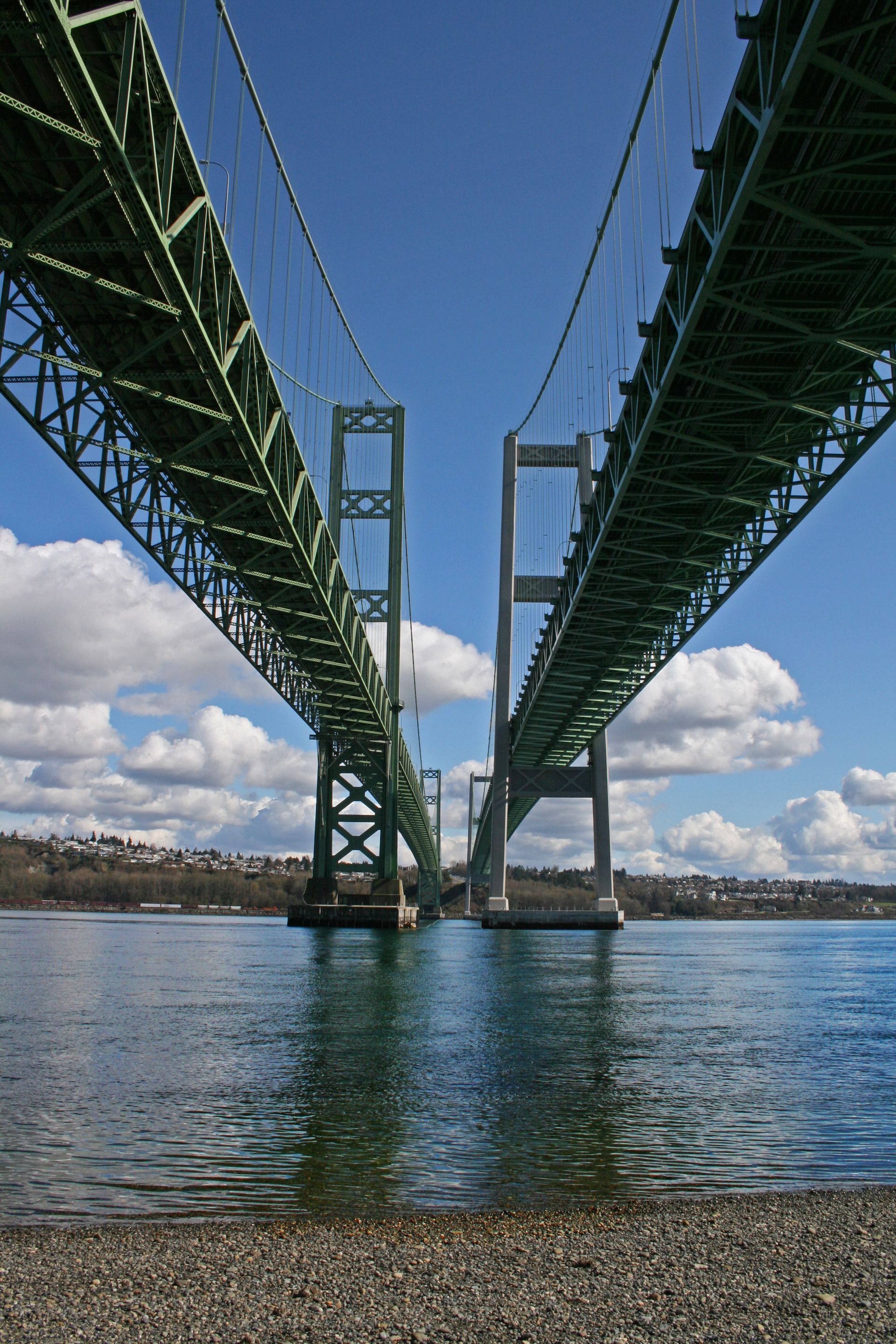 Green suspension bridge over blue water under a partly cloudy sky.