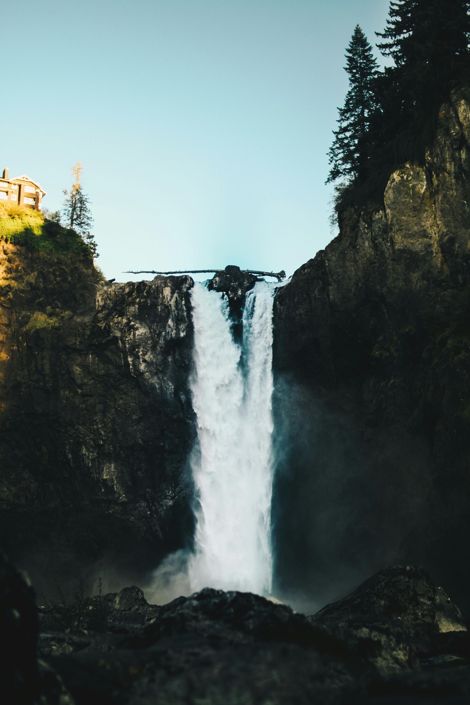 Waterfall cascading over dark rocks under a blue sky.
