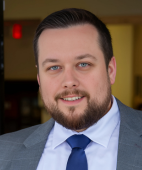 A man with a beard wearing a suit and tie is smiling for the camera.
