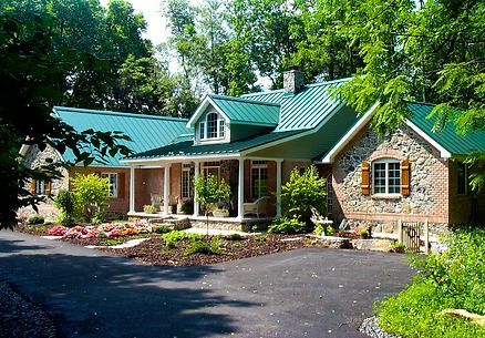 Stone and brick house with a bright green metal roof, surrounded by trees and a circular driveway.