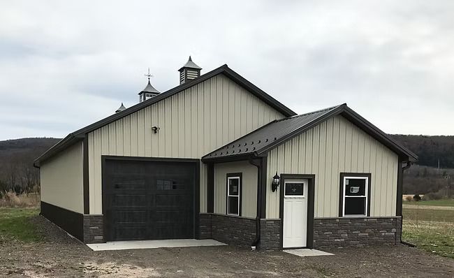 Barn-style building with beige siding, a dark gray garage door, and a smaller, attached structure with a white door.