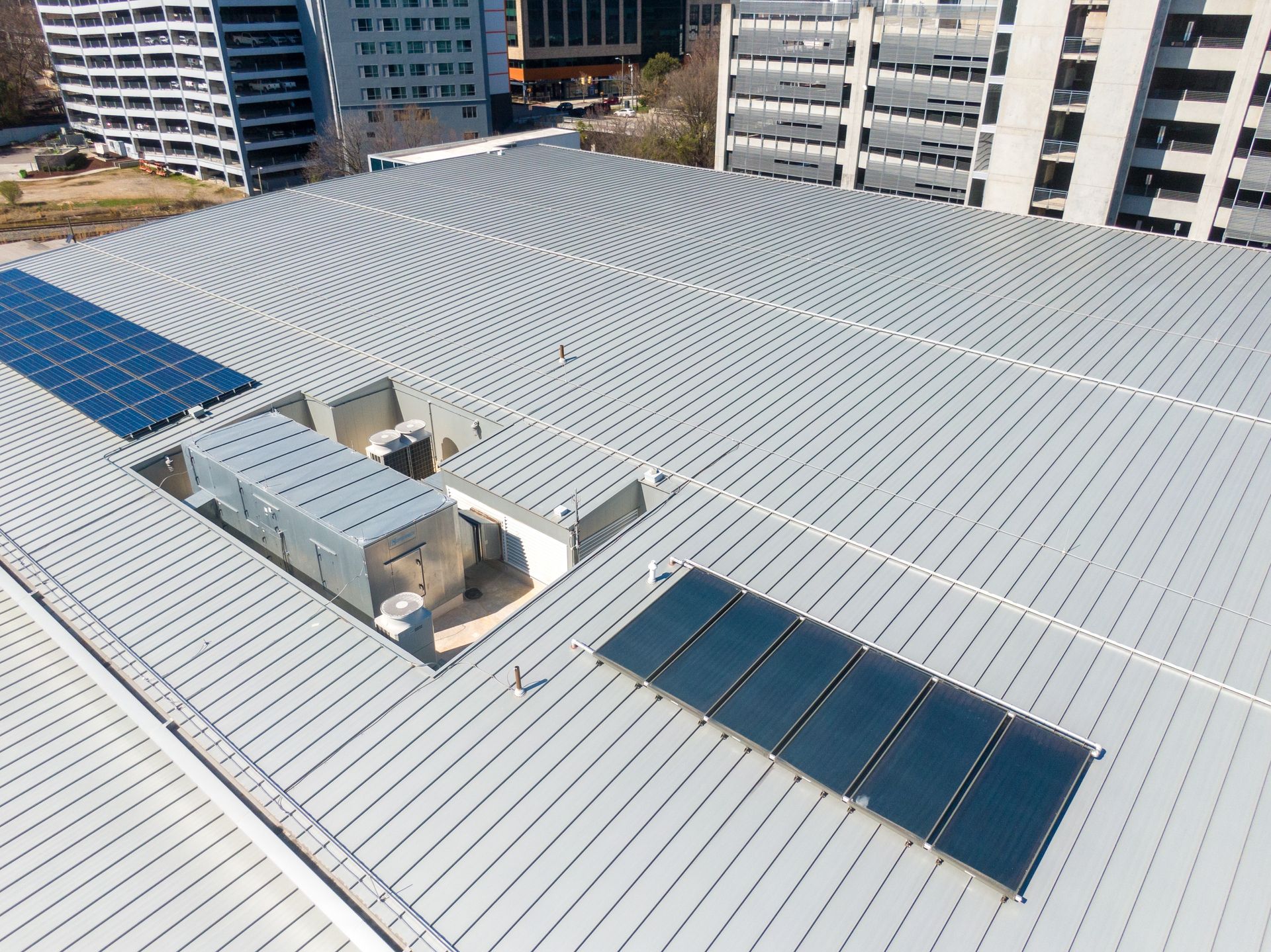 Rooftop with metal panels and solar panels, in a city with tall buildings.