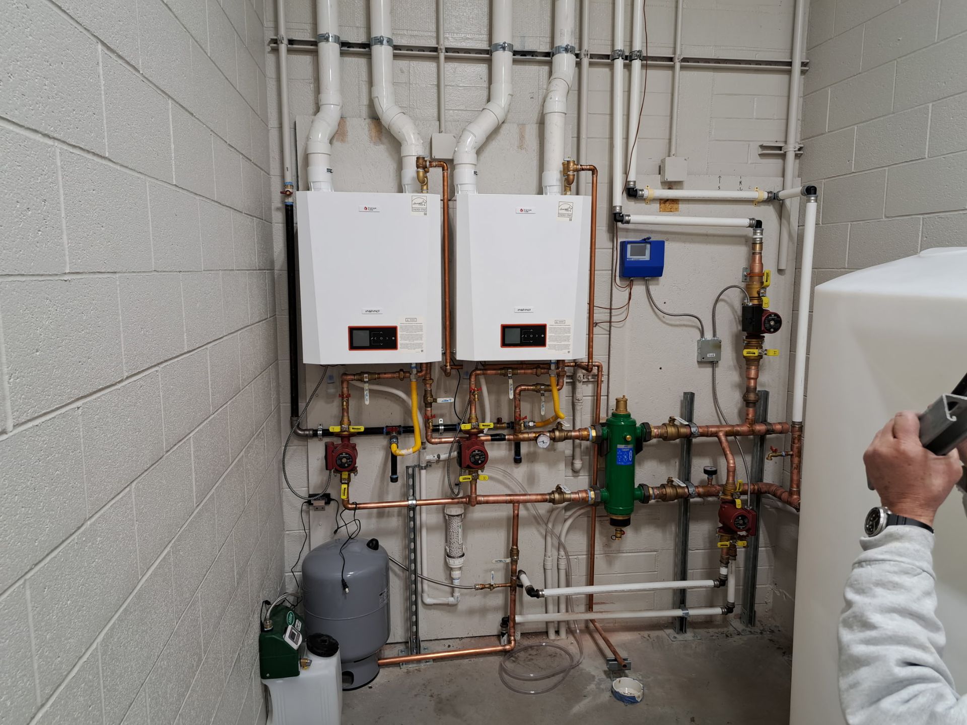 A man is taking a picture of a room with two boilers and pipes.