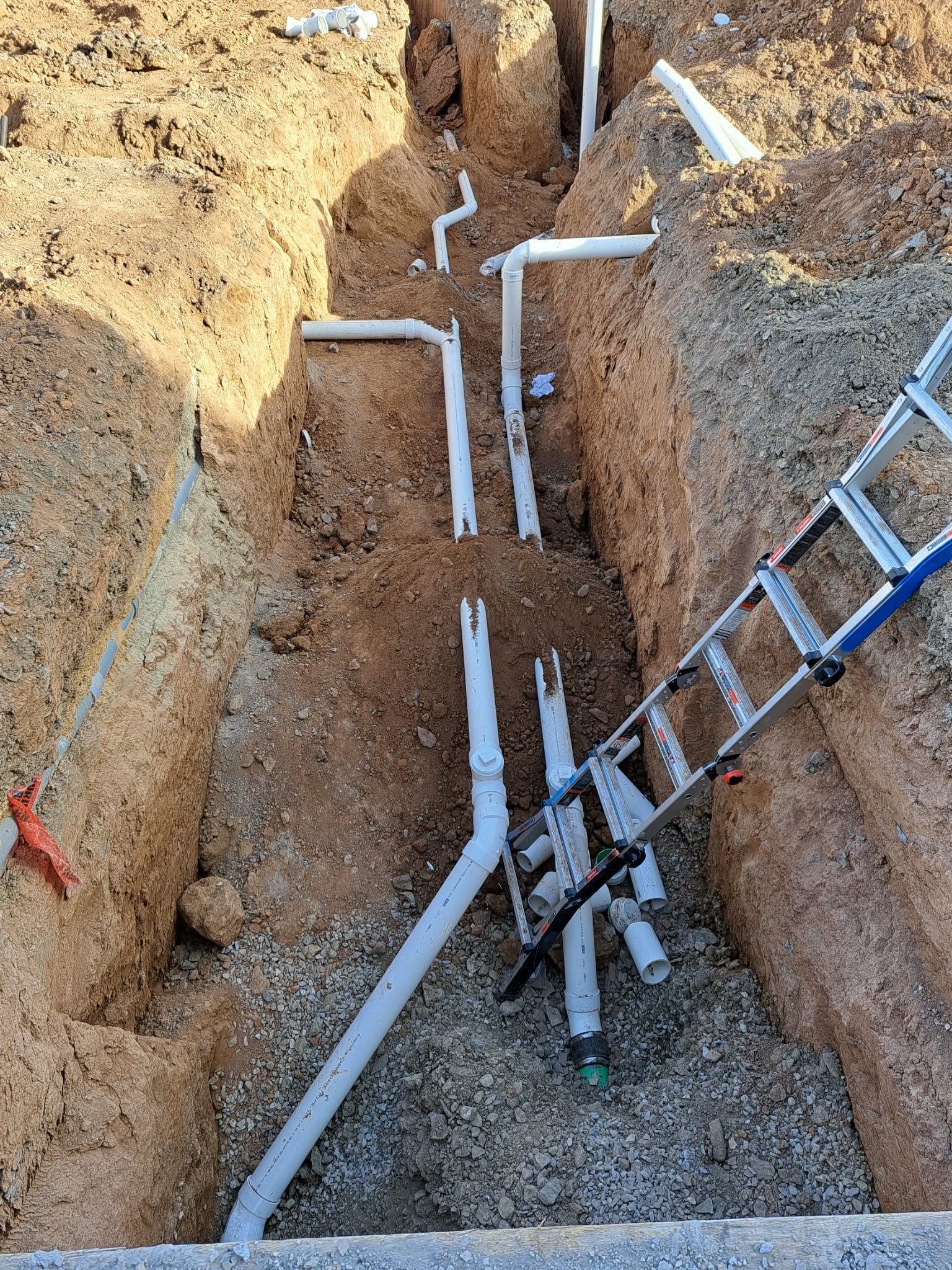 A ladder is sitting in the dirt next to a bunch of pipes.