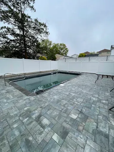 Backyard with a rectangular swimming pool and grey stone pavers, enclosed by a white fence.