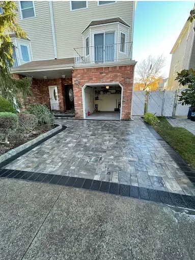 Paver driveway in front of a brick garage with a house in the background.