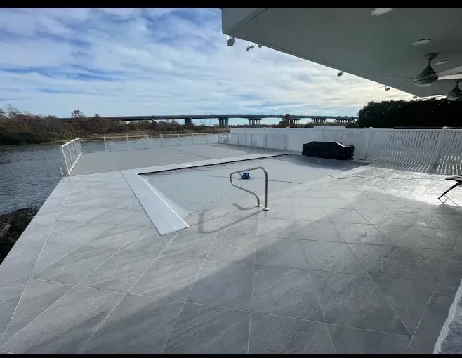 Poolside patio with a view of a river and bridge, featuring a covered pool and white railings.