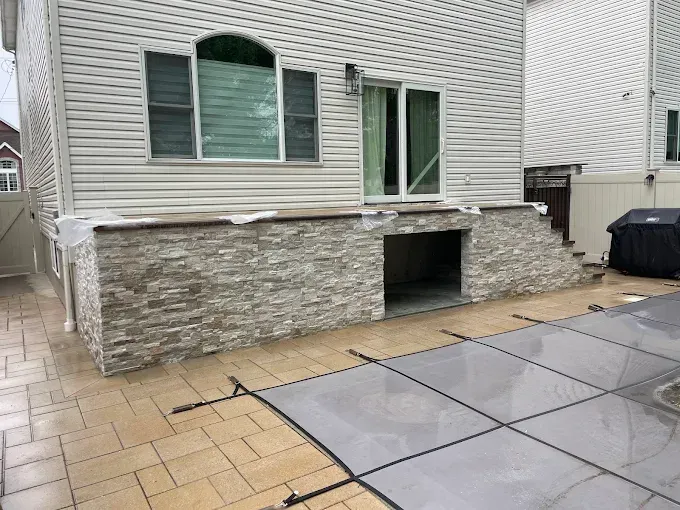 Exterior of a house with stone veneer on a patio, sliding door, and an arched window.