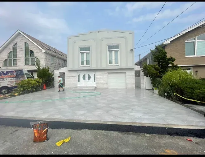 House with light grey facade, new concrete driveway. Man stands on drive.