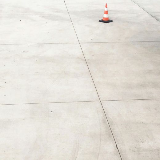 Orange and white traffic cone on a light gray concrete surface with joint lines.