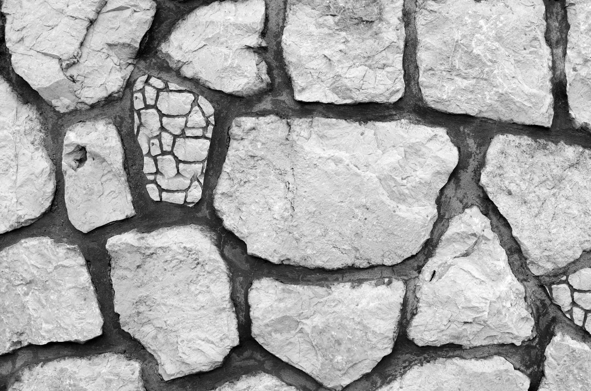 Gray stone wall with irregularly shaped rocks and dark grout.