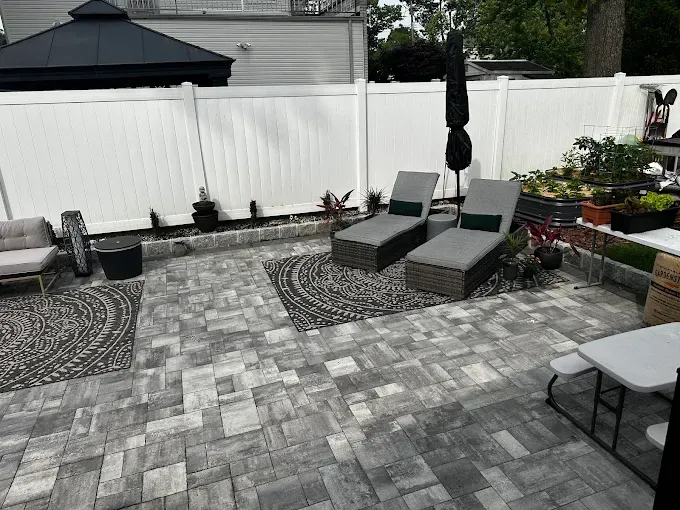 Backyard patio with lounge chairs, grey pavers, white fence, and a gazebo.