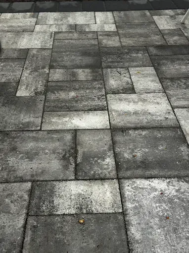 Gray rectangular pavers forming a patio floor. Some have darker staining and uneven wear.