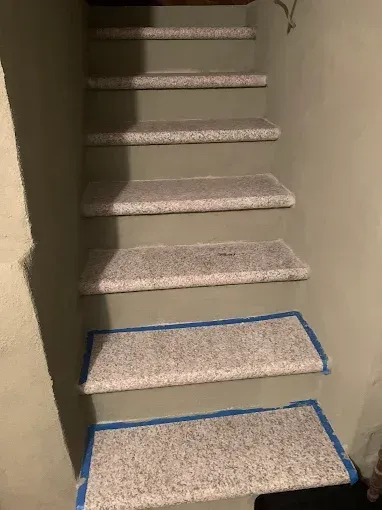 Staircase with gray and white speckled carpeted treads, blue tape along edges.