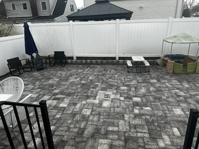 Patio with gray brick pavers, white fence, black furniture, and a gazebo.