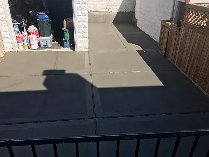 Freshly poured concrete patio, with a garage and fence in the background.