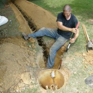 A man is sitting in a hole in the ground holding a shovel.