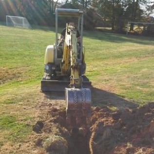 A man is driving a small excavator in a field.