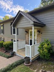 The exterior of a house featuring a grey-sided facade with stone accents, a small covered porch, and white railings.