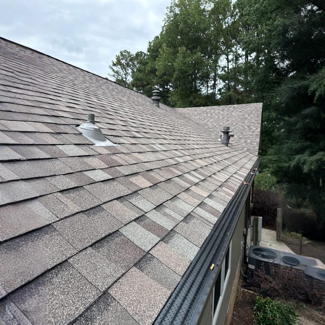 A shingled roof viewed from an elevated angle, featuring two plumbing vent pipes and a gutter guard along the edge.