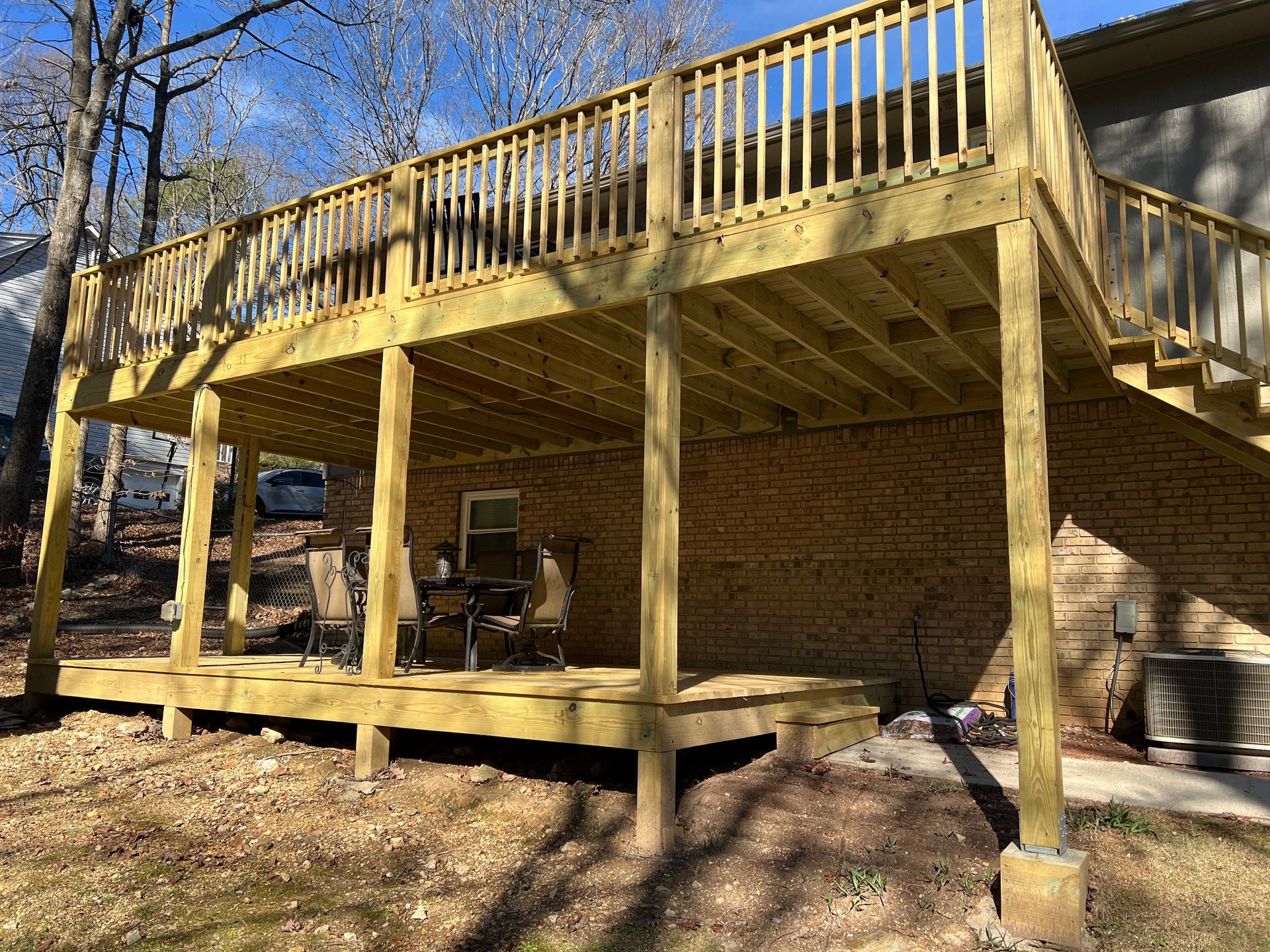 A two-story wooden deck with railings attached to a brick house, overlooking a yard with trees.