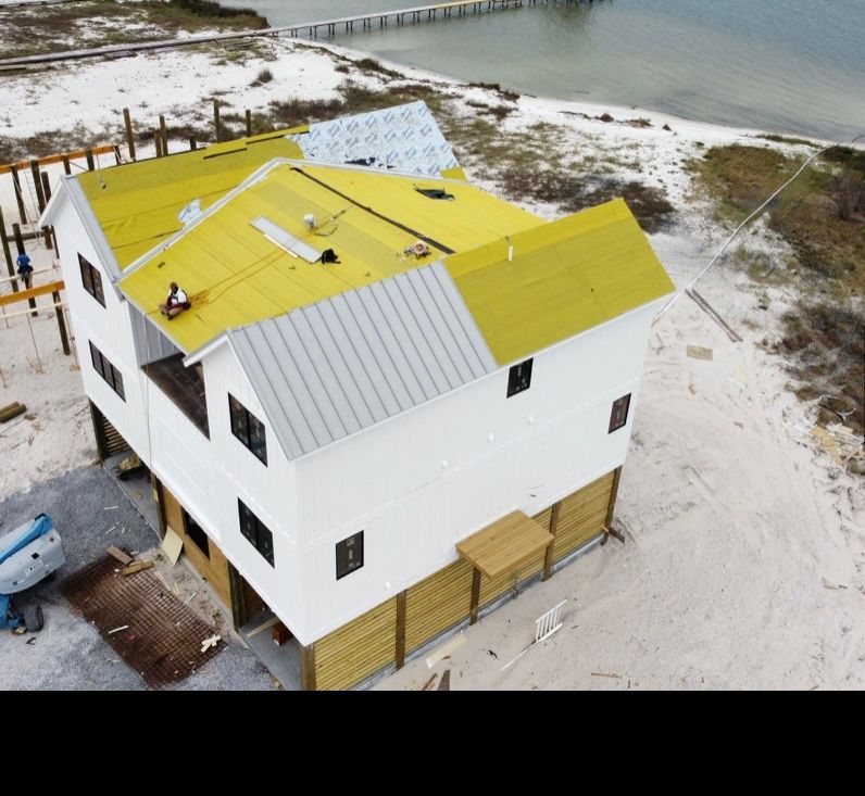An elevated coastal home under construction with a partially installed metal roof and yellow underlayment.