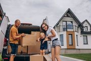 Family unloading cardboard boxes from a van outside a house.