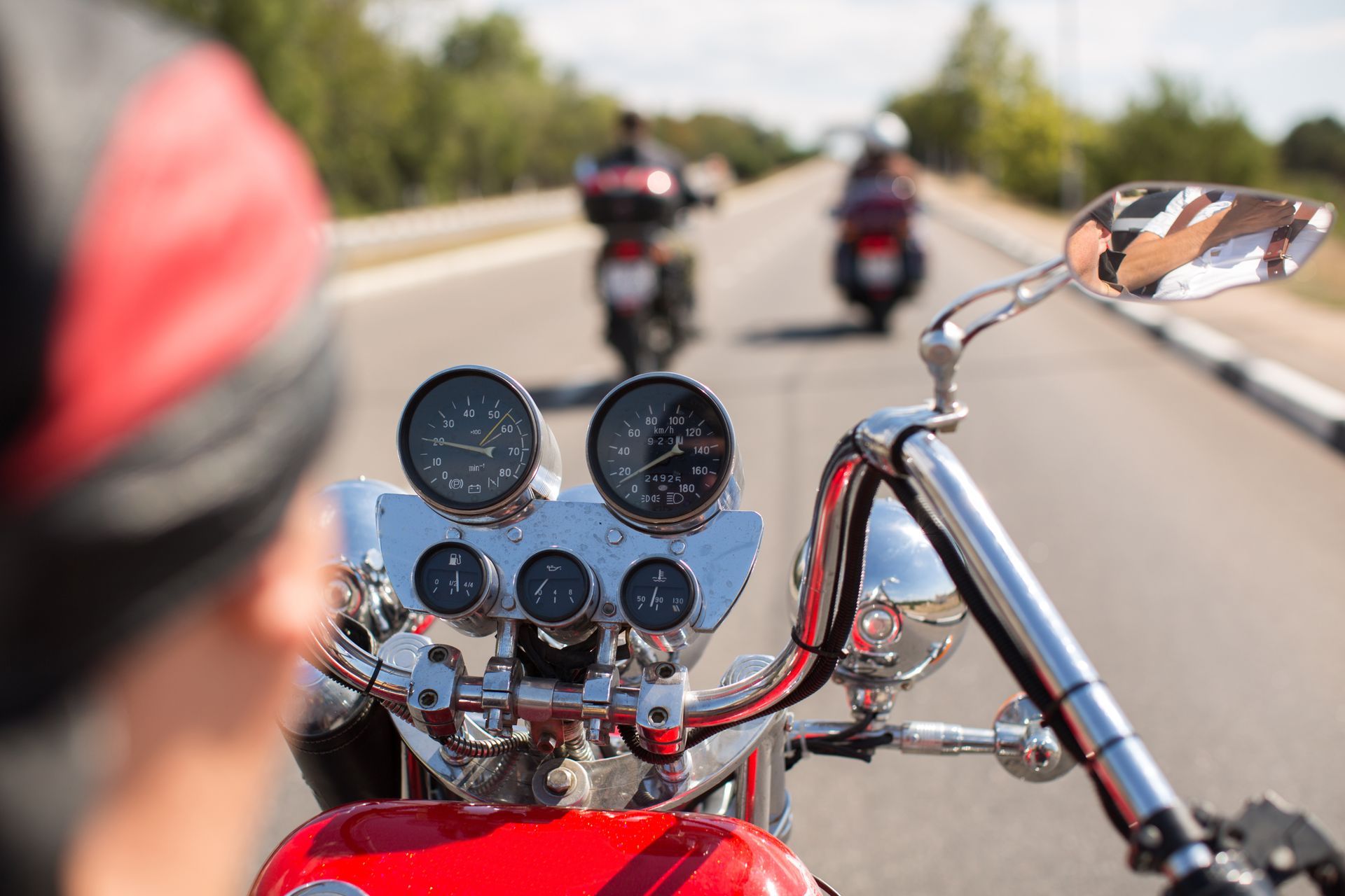 Rider on a red motorcycle on a road, following two bikes ahead in sunlight.