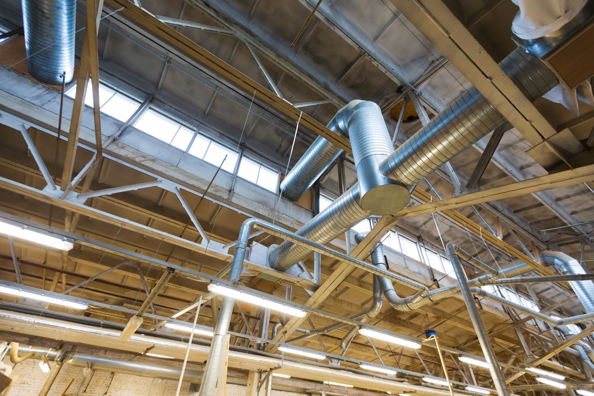Industrial warehouse ceiling with exposed beams, skylights, and silver ventilation ducts