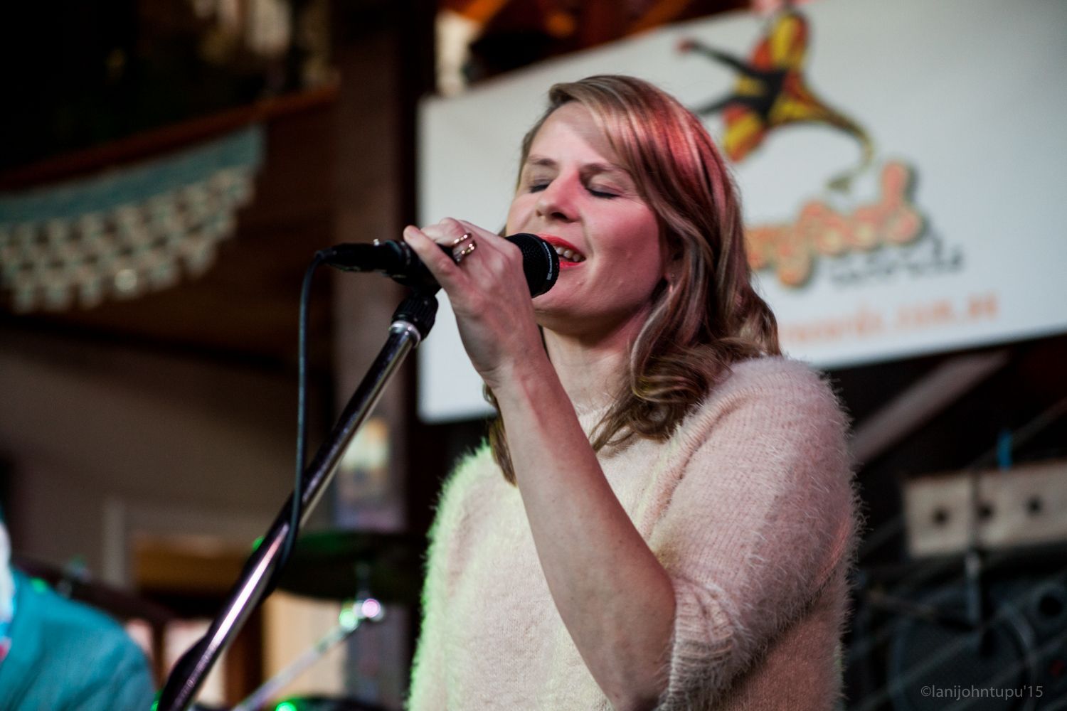 Annie singing into a microphone on stage, eyes closed, wearing a light-colored sweater.