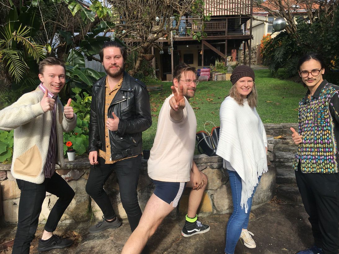 Five people posing outdoors, giving thumbs up and making gestures. Backyard setting with a treehouse.