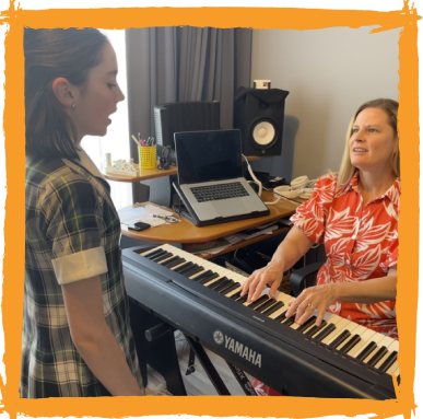 A woman plays piano while a girl sings, inside a home studio.