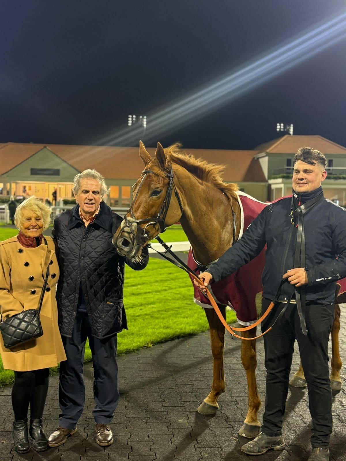 Training Horses with jockeys wearing riding hats and vests riding along a track, near a fence.
