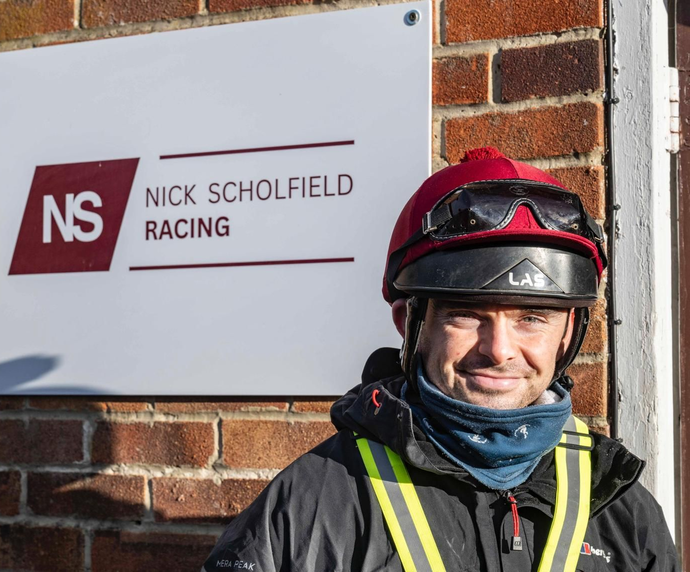 Woman with blonde hair smiles, holding a bay horse in Nick Scholfield's stable.