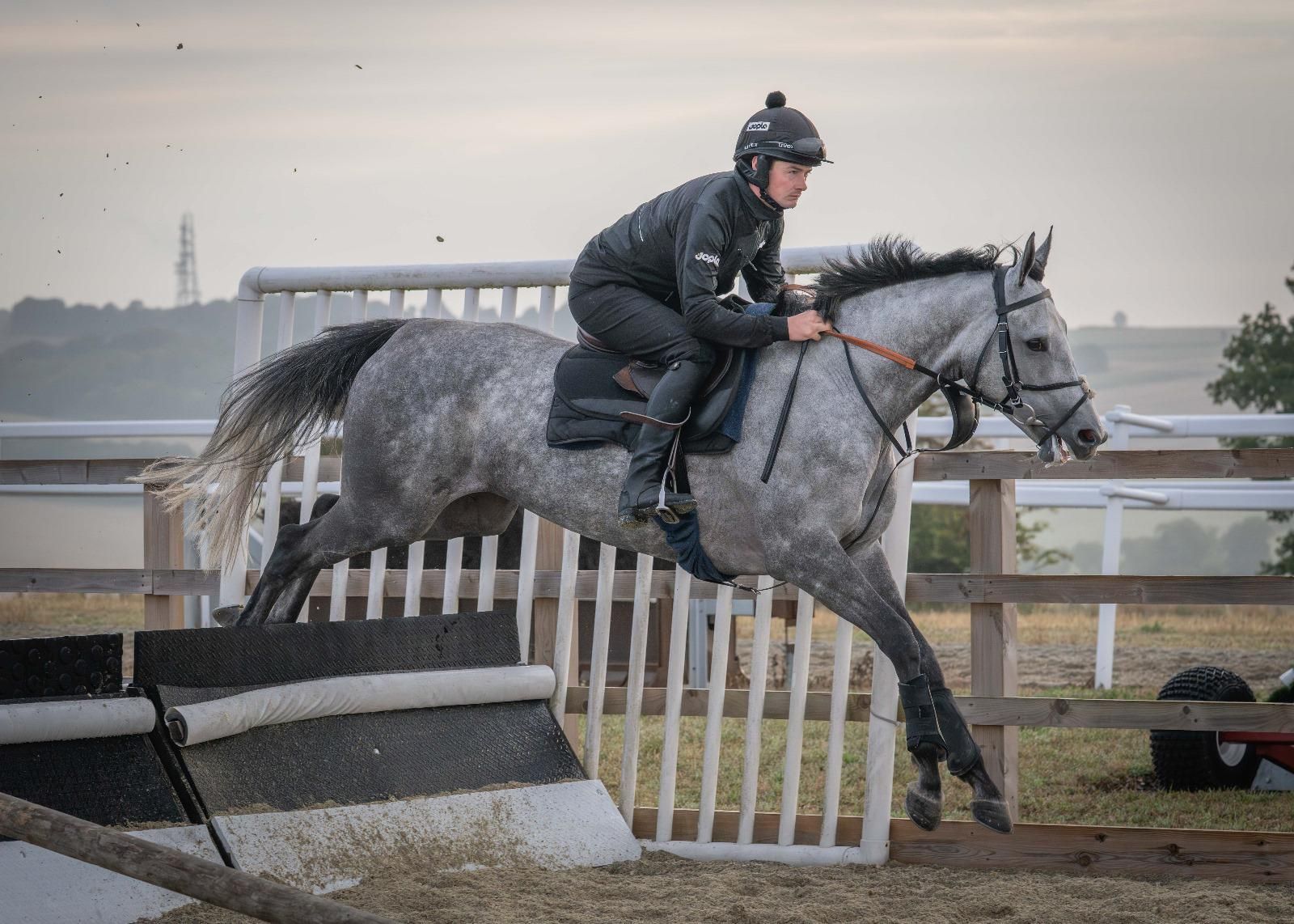 A gray horse and rider jumping over a small fence on a track.