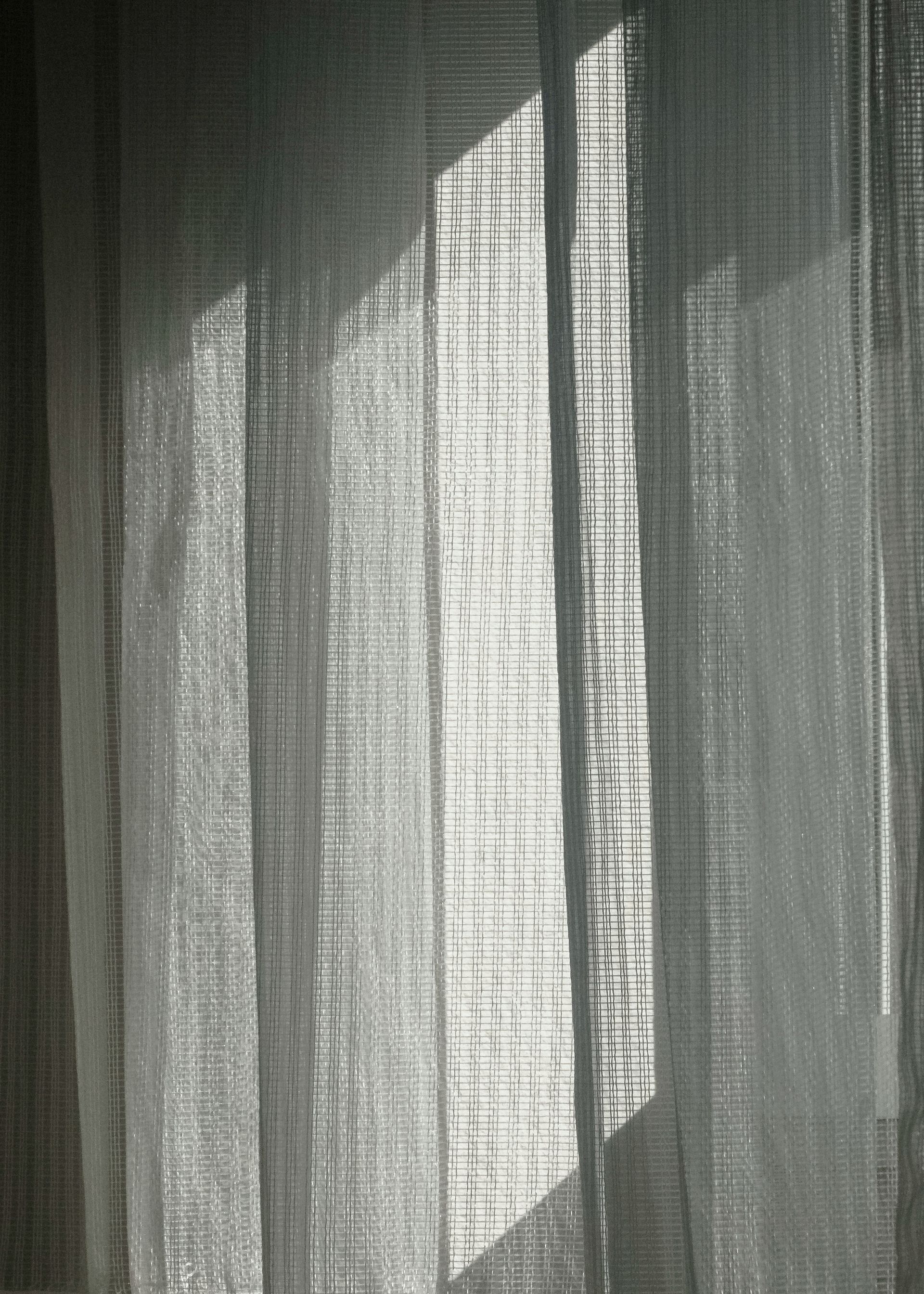 Sheer curtain with bright sunlight shining through, creating shadow patterns.